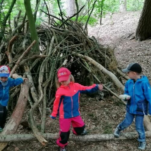 drei Kinder spielen vor einem Tipi im Wald