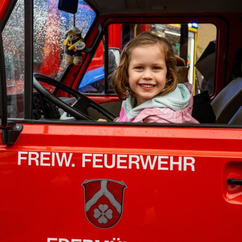 Kind schaut lachend aus Fenster eines Feuerwehrfahrzeugs